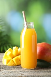 Photo of Tasty mango juice in glass bottle and fresh fruits on wooden table against blurred background