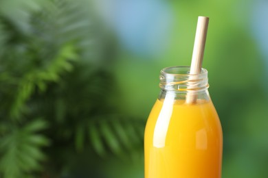 Photo of Tasty mango juice in glass bottle on blurred background, closeup. Space for text