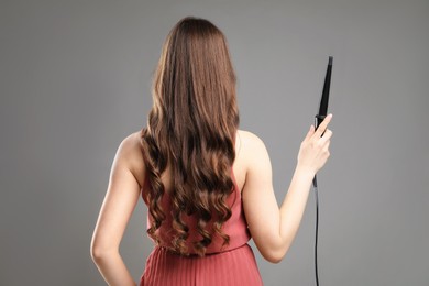Photo of Woman with beautiful hairstyle and curling iron on grey background, back view