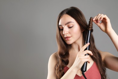 Photo of Beautiful woman curling her hair on grey background. Space for text