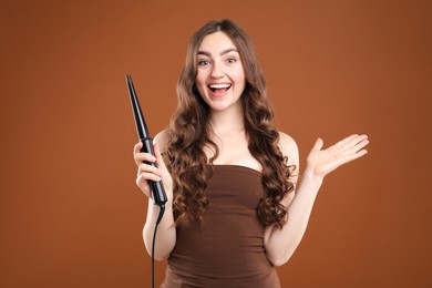 Photo of Woman curling her beautiful hair on brown background