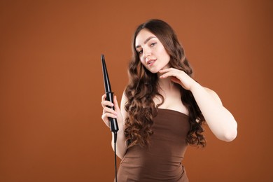 Photo of Woman curling her beautiful hair on brown background. Space for text