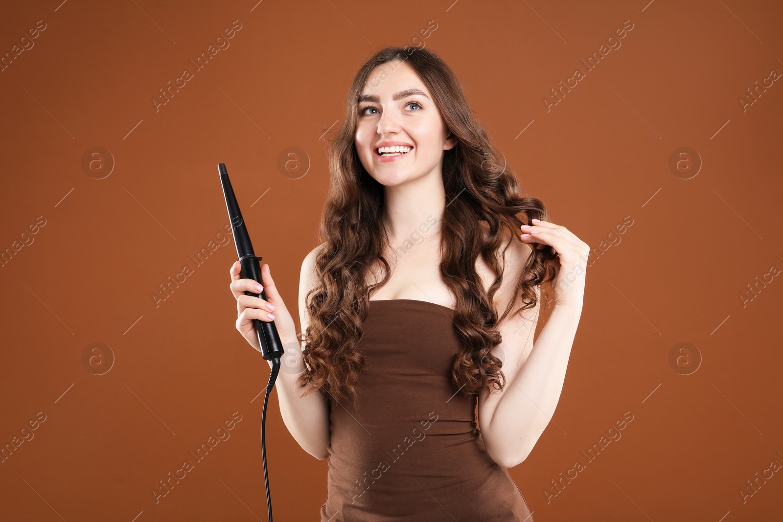 Photo of Woman curling her beautiful hair on brown background