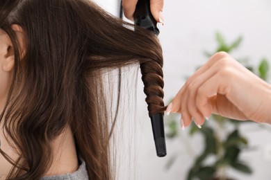 Photo of Hairdresser curling woman's hair in salon, closeup