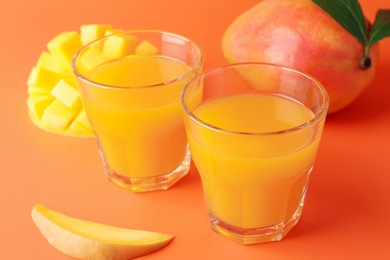 Photo of Tasty mango juice in glasses and fresh fruits on orange background, closeup