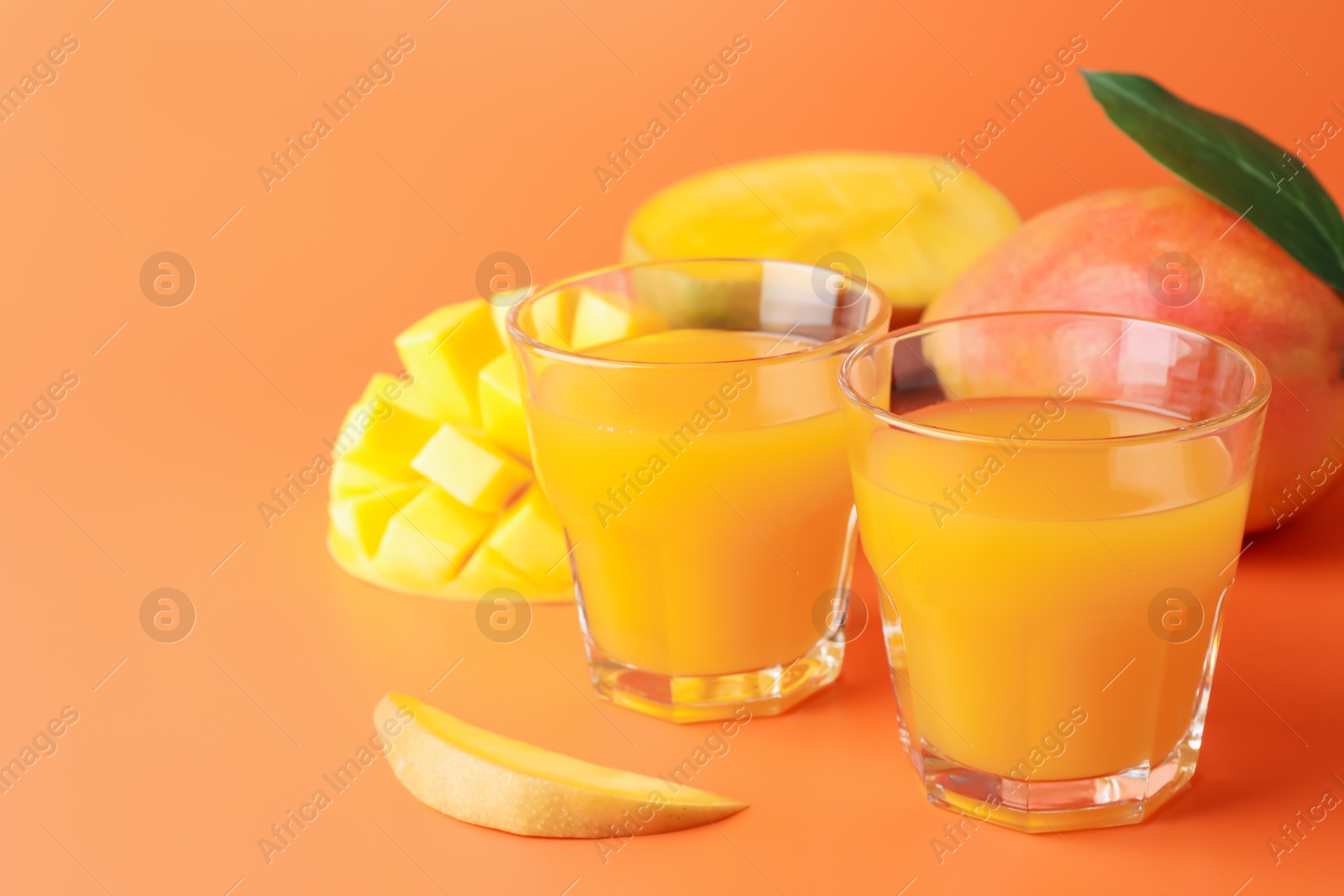 Tasty mango juice in glasses and fresh fruits on orange background, closeup. Space for text Photo of Tasty mango juice in glasses and fresh fruits on orange background, closeup. Space for text