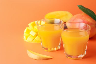 Photo of Tasty mango juice in glasses and fresh fruits on orange background, closeup. Space for text