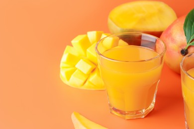 Photo of Tasty mango juice in glass and fresh fruits on orange background, closeup. Space for text
