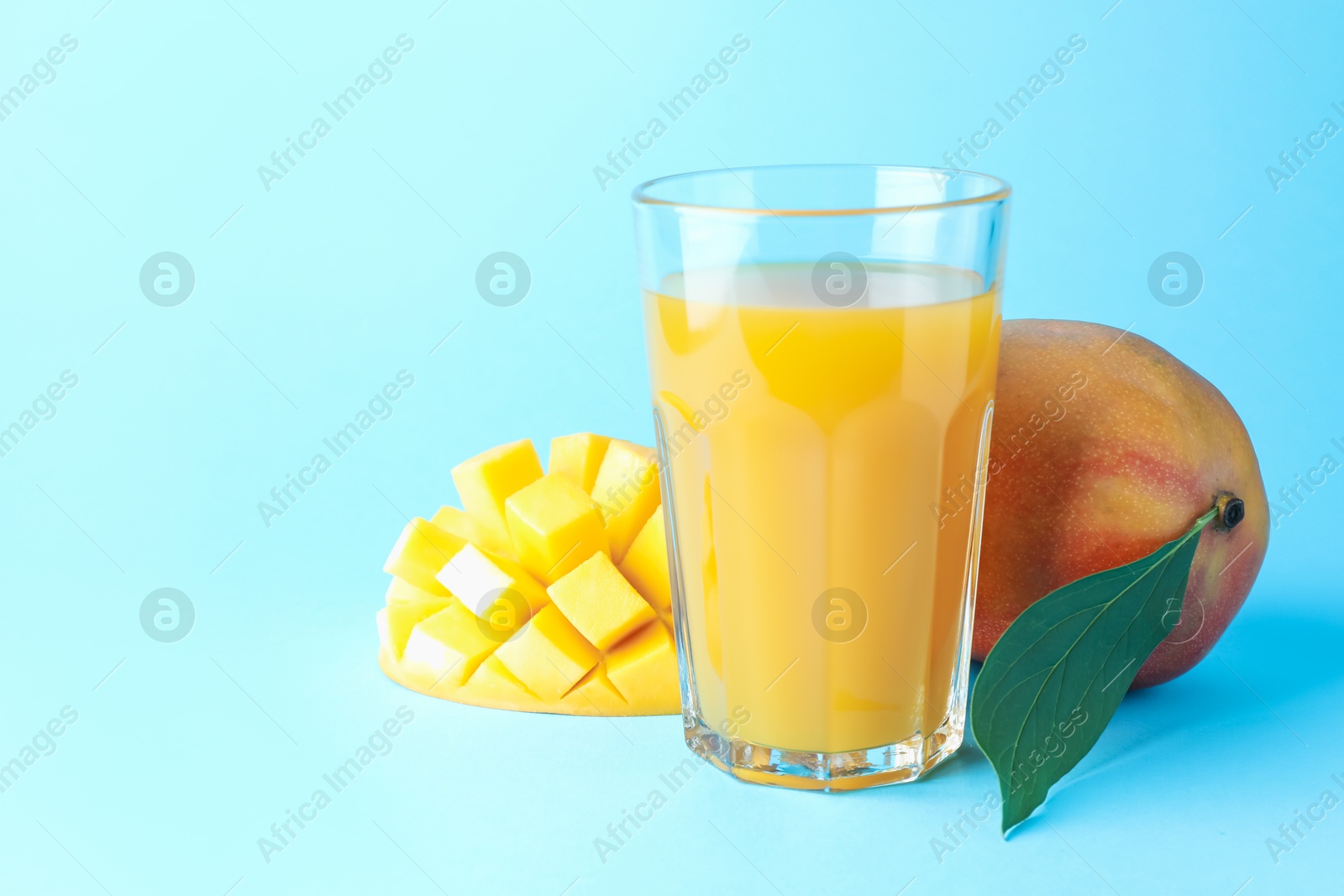Tasty mango juice in glass and fresh fruits on light blue background, space for text Photo of Tasty mango juice in glass and fresh fruits on light blue background, space for text