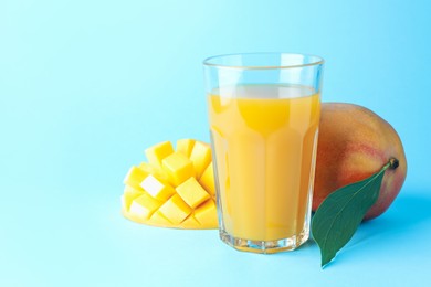 Photo of Tasty mango juice in glass and fresh fruits on light blue background, space for text