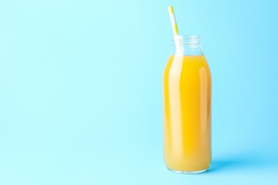 Photo of Tasty mango juice in glass bottle on light blue background, space for text