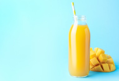 Photo of Tasty mango juice in glass bottle and fresh fruit on light blue background, space for text