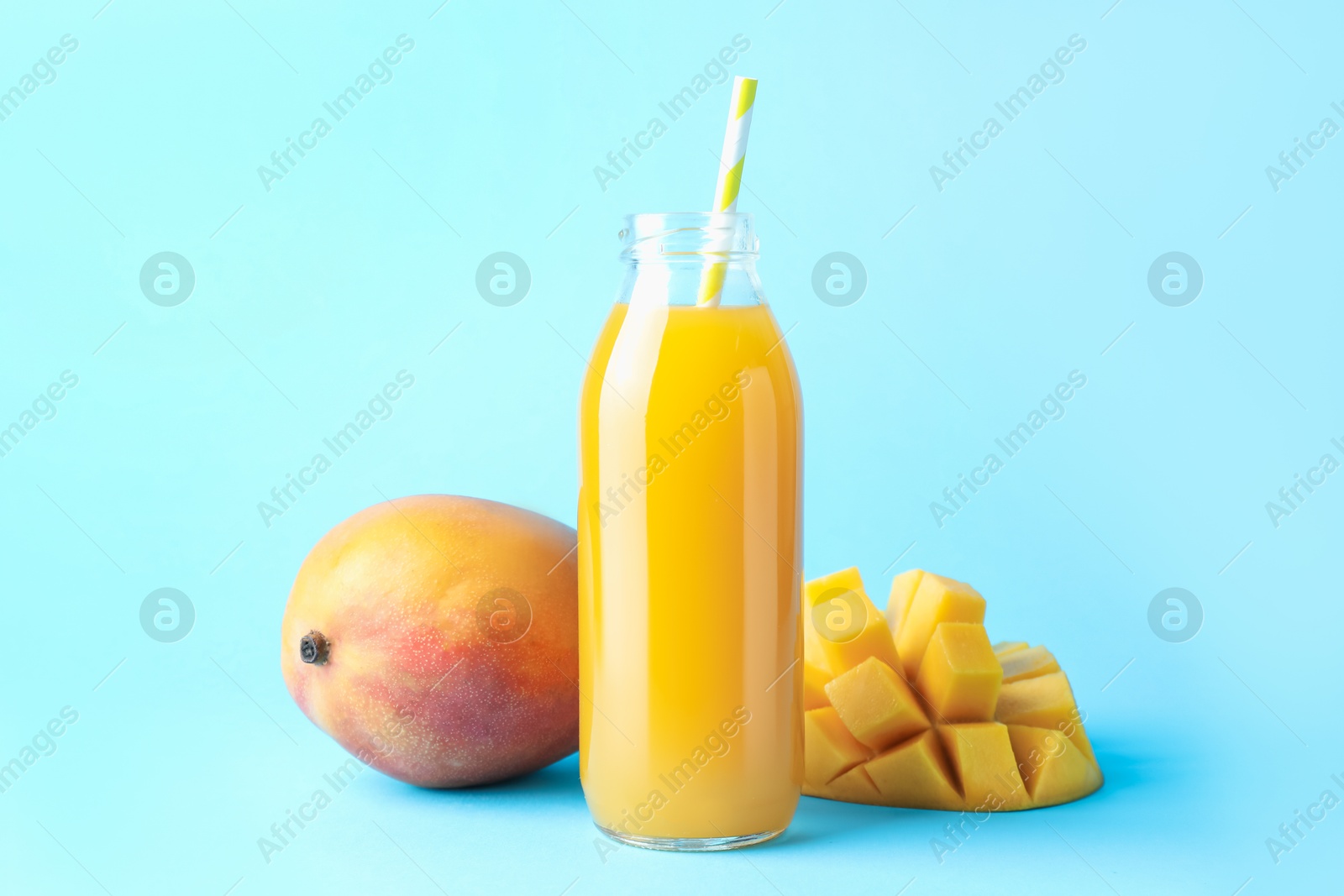 Tasty mango juice in glass bottle and fresh fruits on light blue background Photo of Tasty mango juice in glass bottle and fresh fruits on light blue background