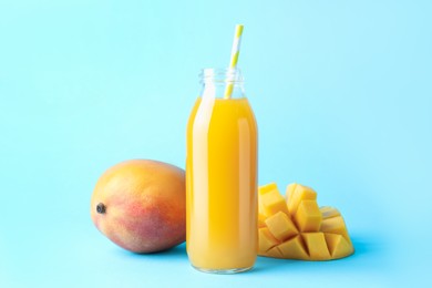 Photo of Tasty mango juice in glass bottle and fresh fruits on light blue background