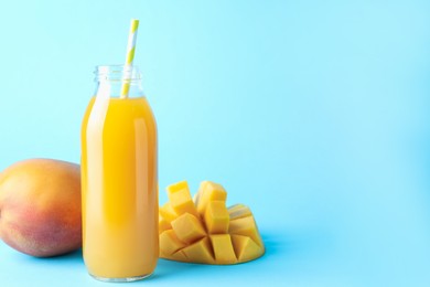 Photo of Tasty mango juice in glass bottle and fresh fruits on light blue background, space for text