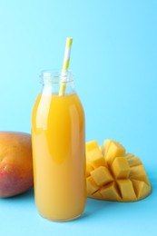 Photo of Tasty mango juice in glass bottle and fresh fruits on light blue background