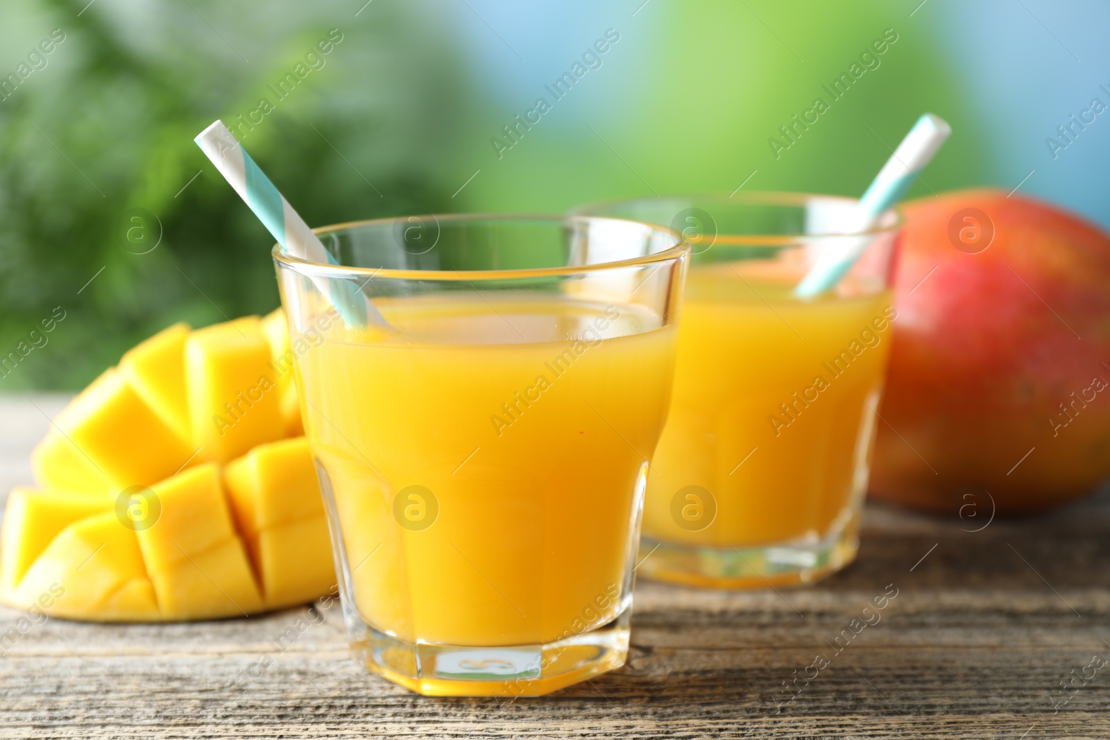 Tasty mango juice in glasses and fresh fruits on wooden table against blurred background, closeup Photo of Tasty mango juice in glasses and fresh fruits on wooden table against blurred background, closeup