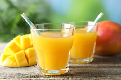 Photo of Tasty mango juice in glasses and fresh fruits on wooden table against blurred background, closeup