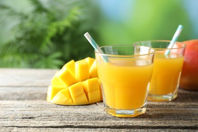 Photo of Tasty mango juice in glasses and fresh fruits on wooden table against blurred background, closeup. Space for text