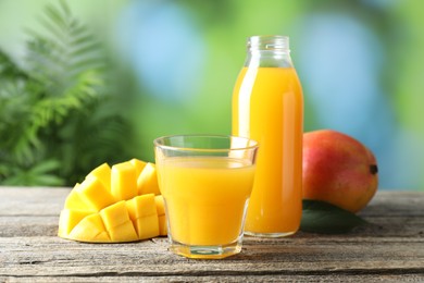 Photo of Tasty mango juice in glass, bottle and fresh fruits on wooden table against blurred background