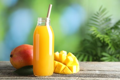 Photo of Tasty mango juice in glass bottle and fresh fruits on wooden table against blurred background, space for text