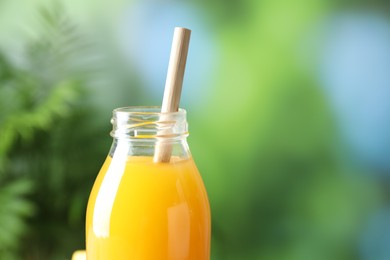 Photo of Tasty mango juice in glass bottle on blurred background, closeup. Space for text