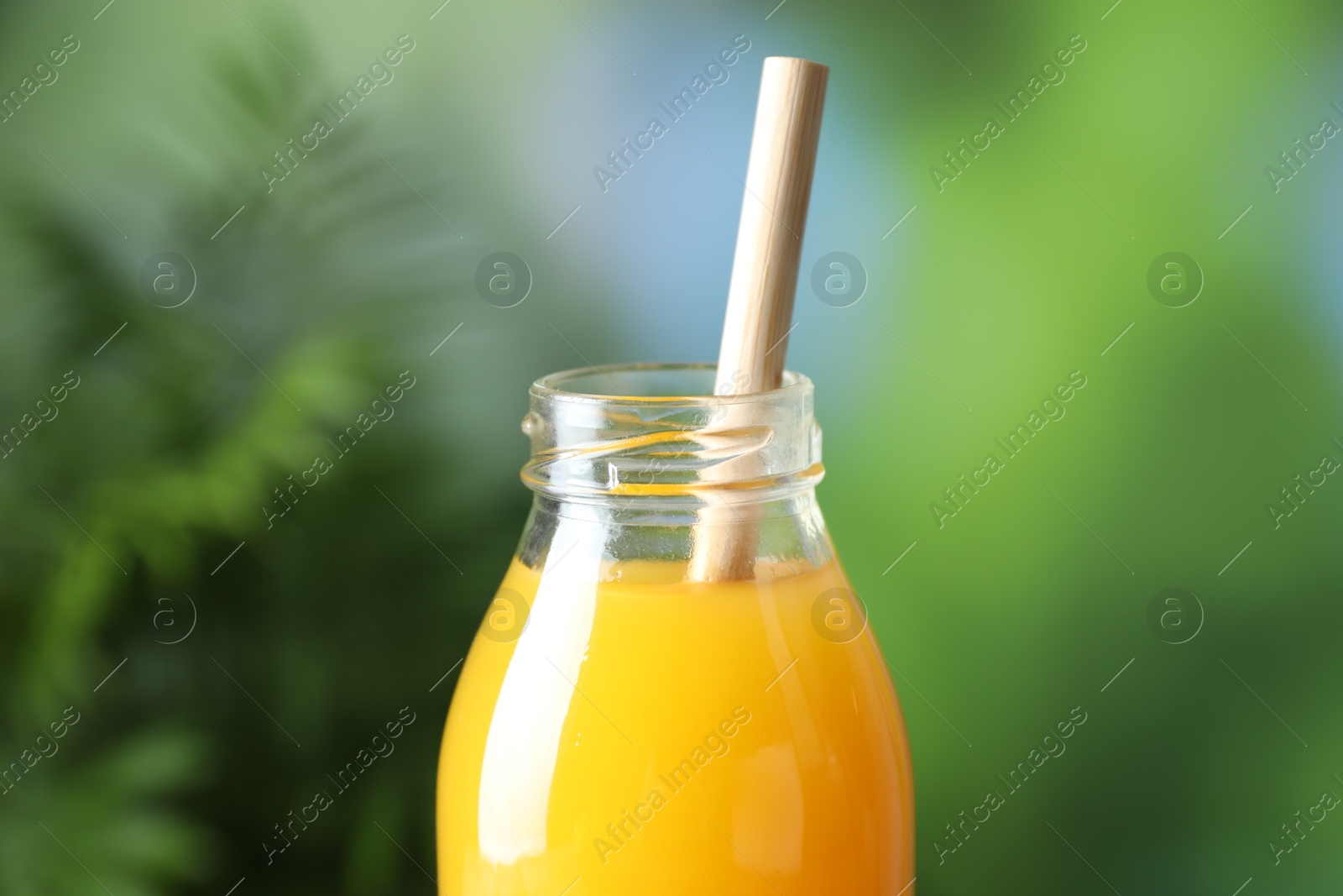 Tasty mango juice in glass bottle on blurred background, closeup Photo of Tasty mango juice in glass bottle on blurred background, closeup