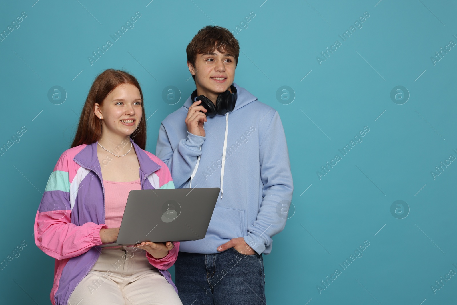 Teenage girl and boy with laptop on light blue background. Space for text Photo of Teenage girl and boy with laptop on light blue background. Space for text