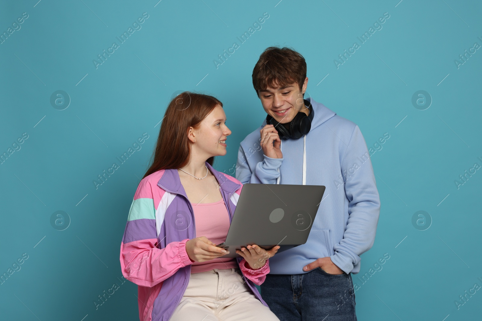 Photo of Teenage girl and boy with laptop on light blue background