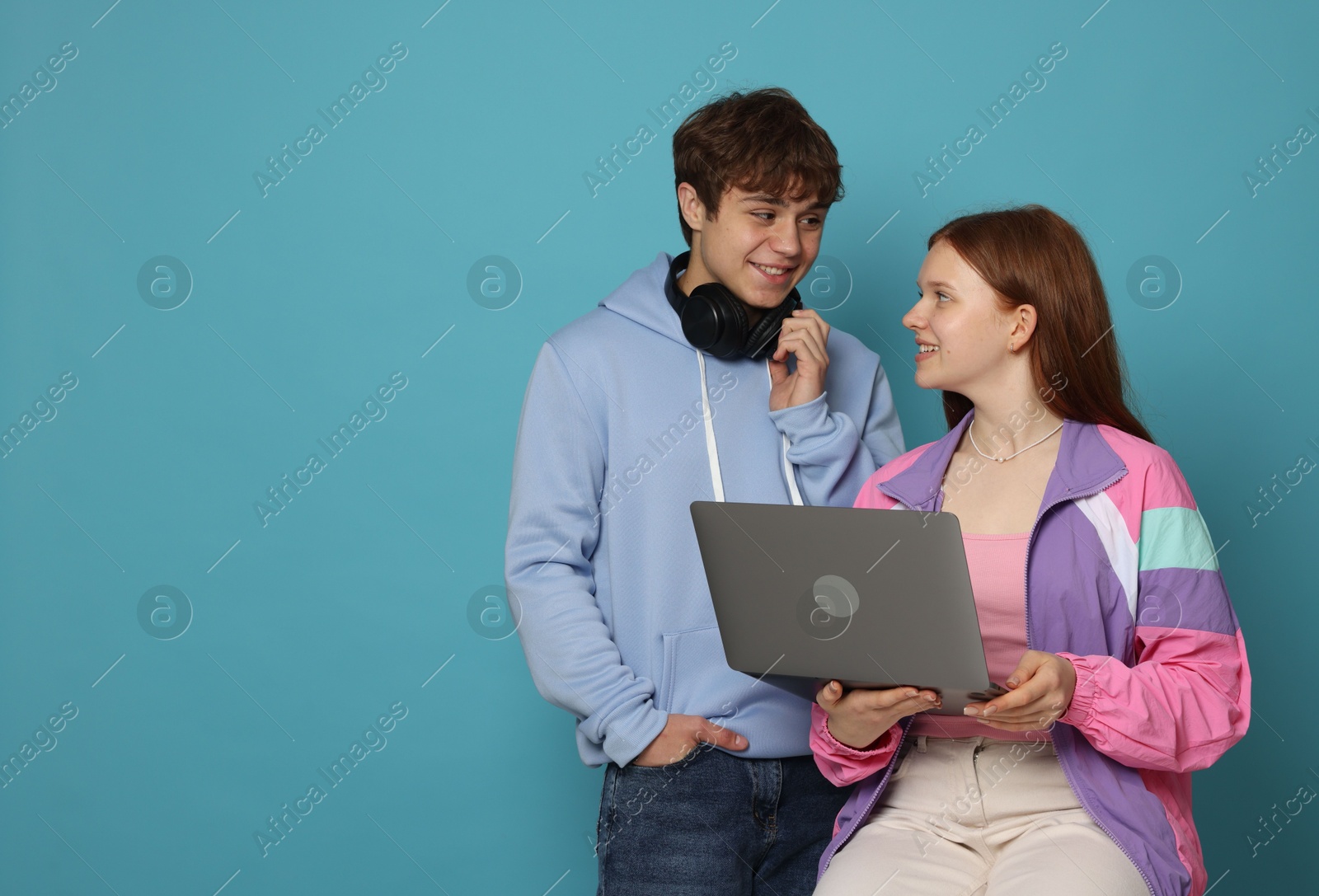 Teenage girl and boy with laptop on light blue background. Space for text Photo of Teenage girl and boy with laptop on light blue background. Space for text