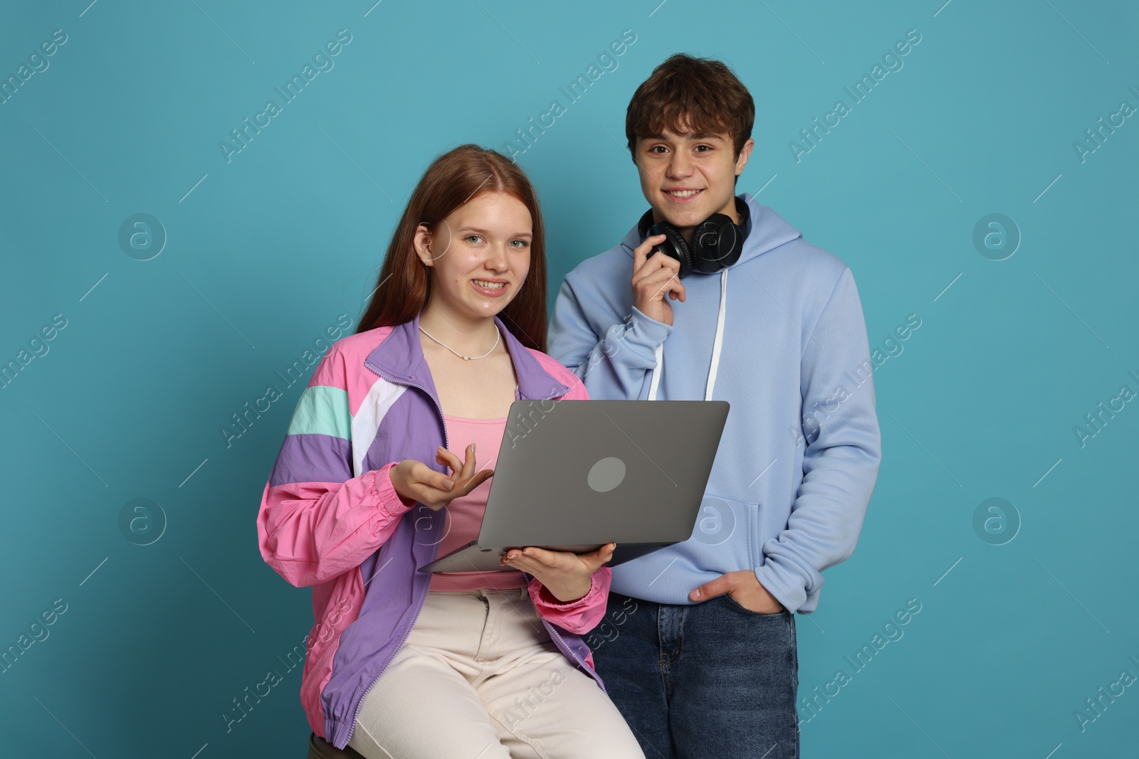 Photo of Teenage girl and boy with laptop on light blue background