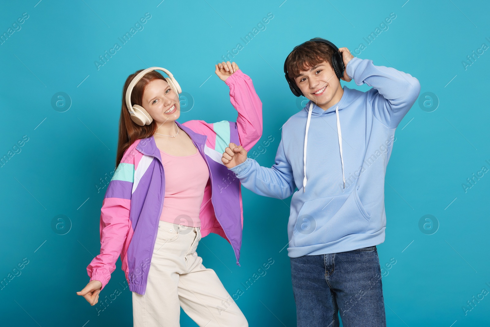 Photo of Teenage girl and boy with headphones dancing on light blue background
