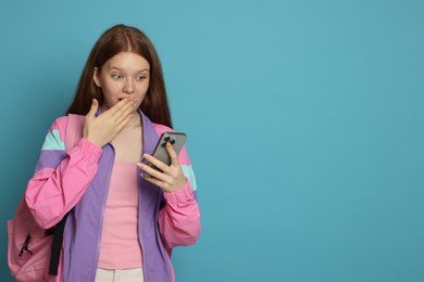 Photo of Surprised teenage girl with smartphone on light blue background. Space for text