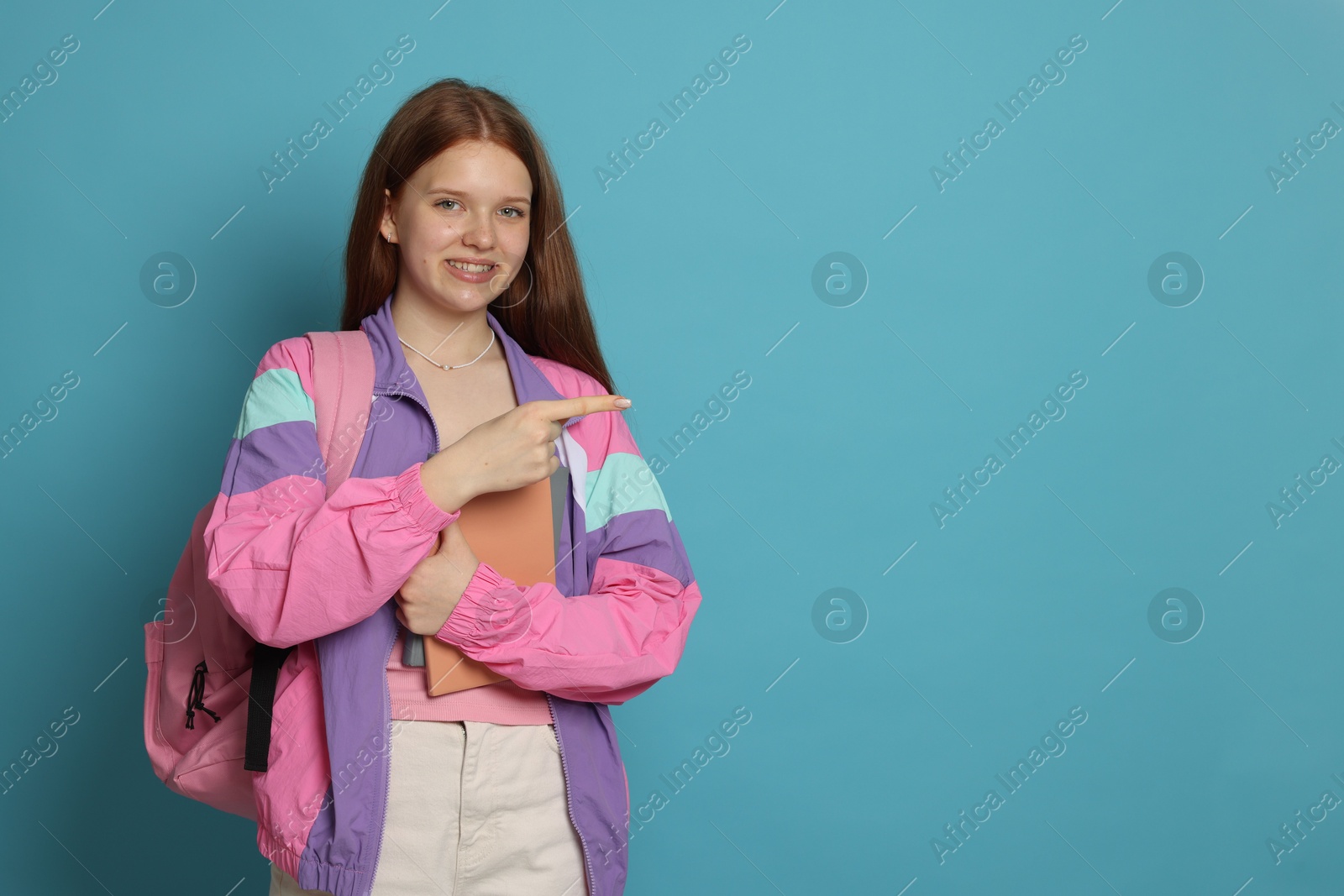 Teenage girl with books pointing at something on light blue background. Space for text Photo of Teenage girl with books pointing at something on light blue background. Space for text