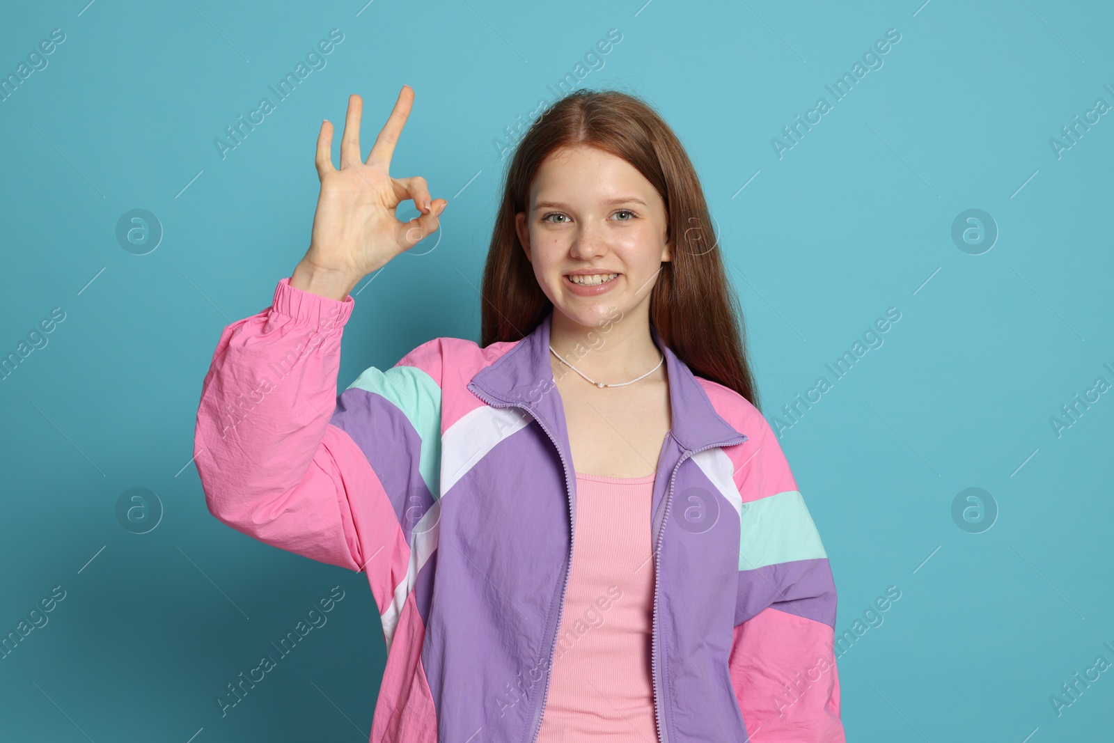 Teenage girl showing okay gesture on light blue background Photo of Teenage girl showing okay gesture on light blue background