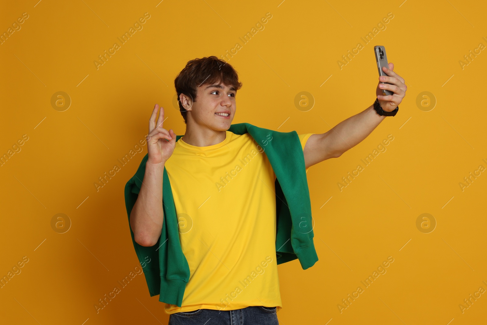 Teenage boy taking selfie on yellow background Photo of Teenage boy taking selfie on yellow background
