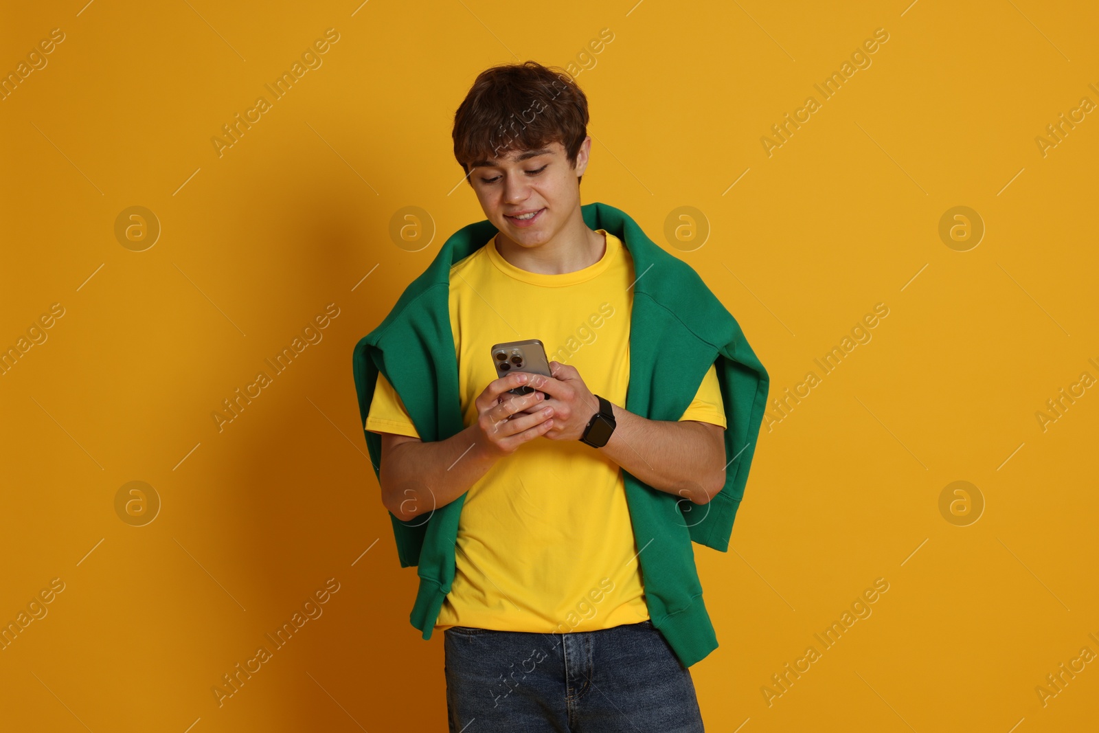 Teenage boy with smartphone on yellow background Photo of Teenage boy with smartphone on yellow background