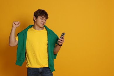 Photo of Excited teenage boy with smartphone on yellow background. Space for text