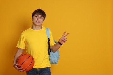 Photo of Teenage boy with basketball on yellow background. Space for text