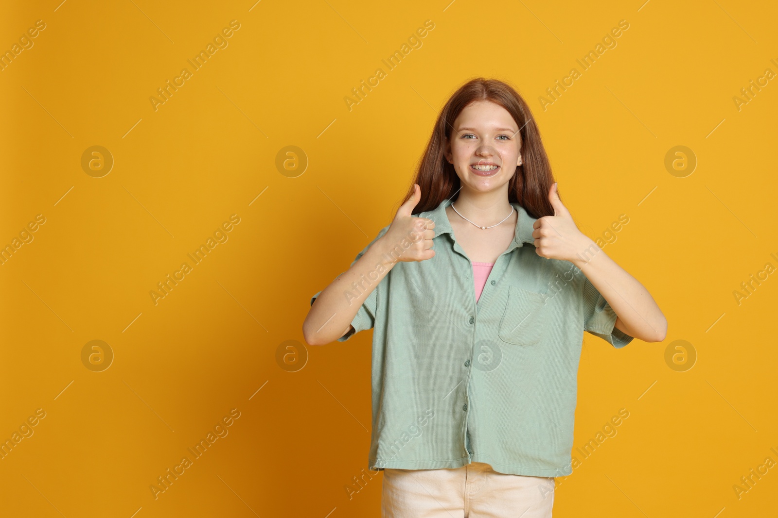Photo of Teenage girl showing thumbs ups on yellow background. Space for text