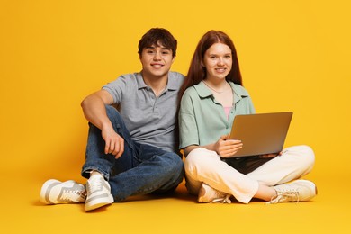 Photo of Teenage girl and boy with laptop on yellow background