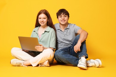 Photo of Teenage girl and boy with laptop on yellow background