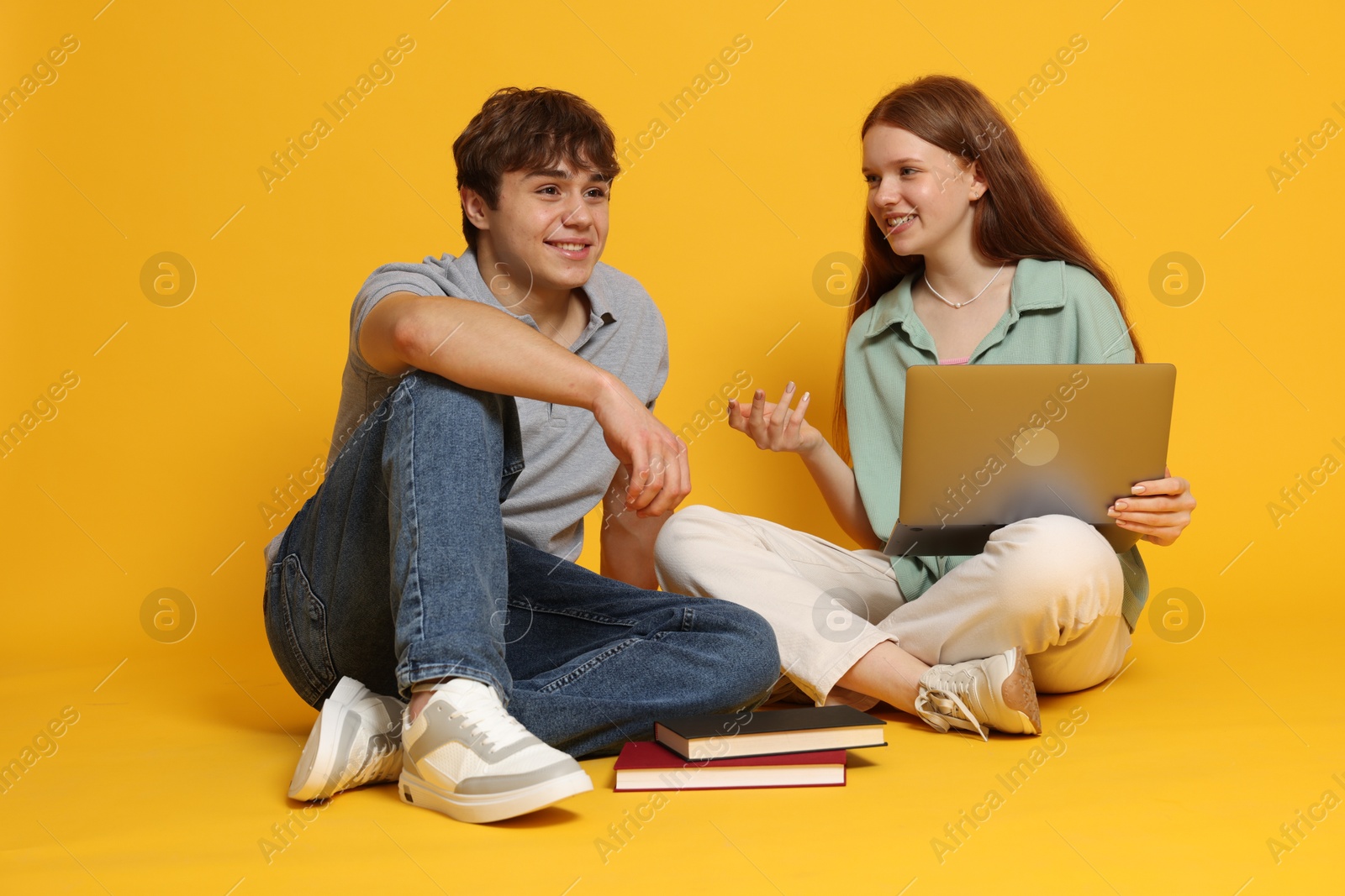 Photo of Teenage girl and boy with laptop on yellow background