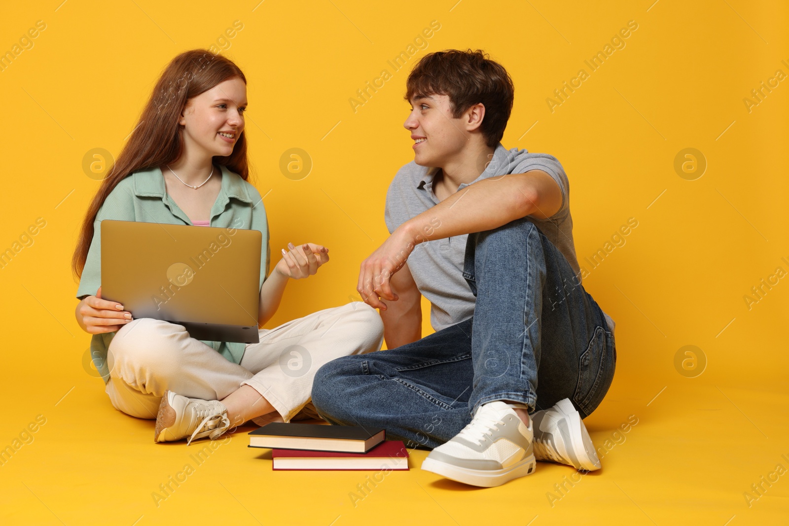 Teenage girl and boy with laptop on yellow background Photo of Teenage girl and boy with laptop on yellow background