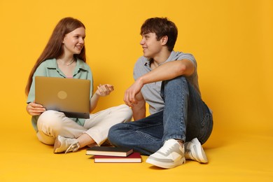 Photo of Teenage girl and boy with laptop on yellow background