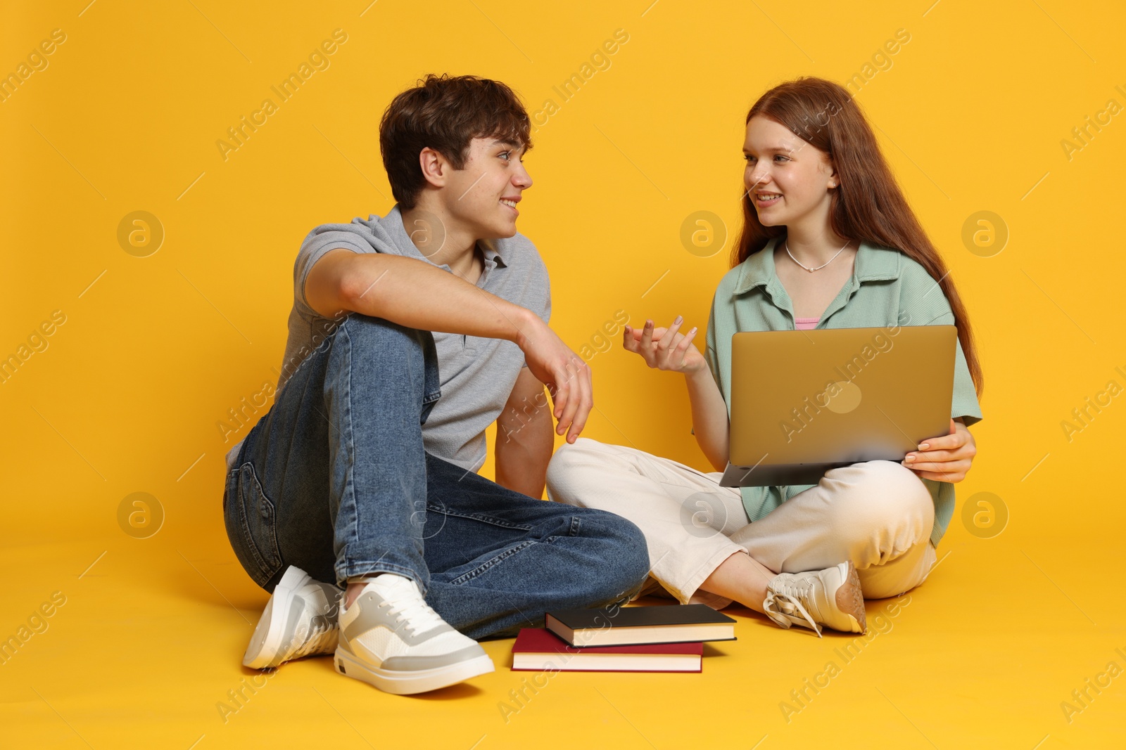 Teenage girl and boy with laptop on yellow background Photo of Teenage girl and boy with laptop on yellow background