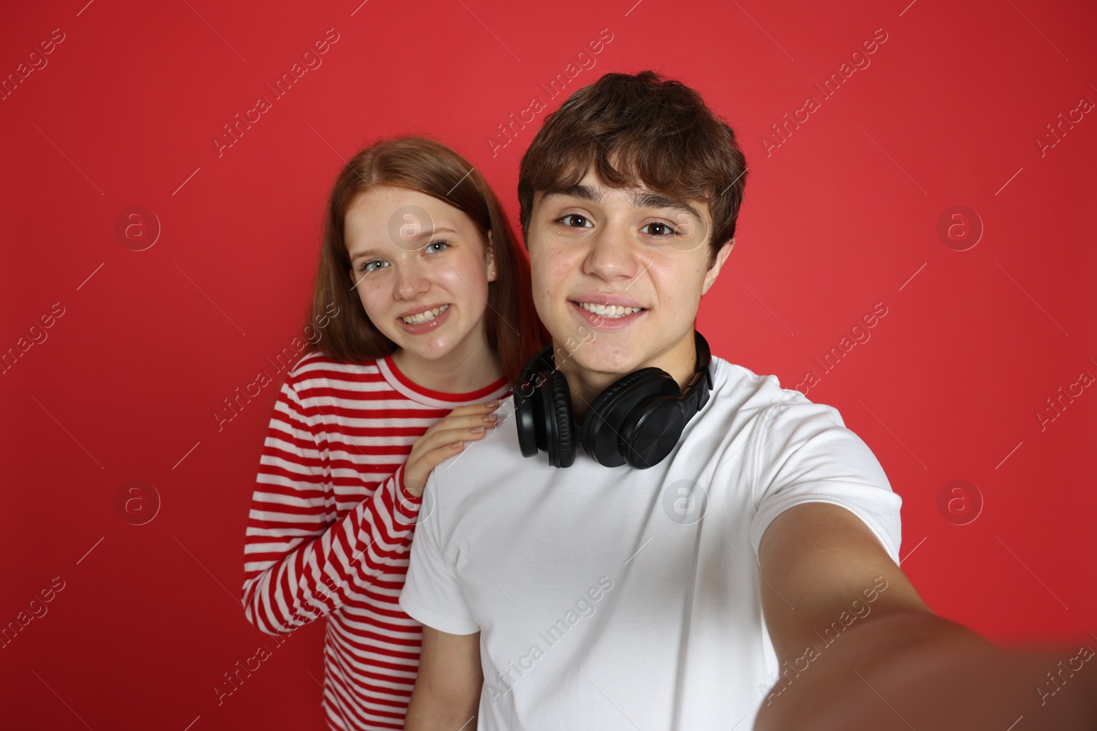 Photo of Teenage girl and boy taking selfie on red background