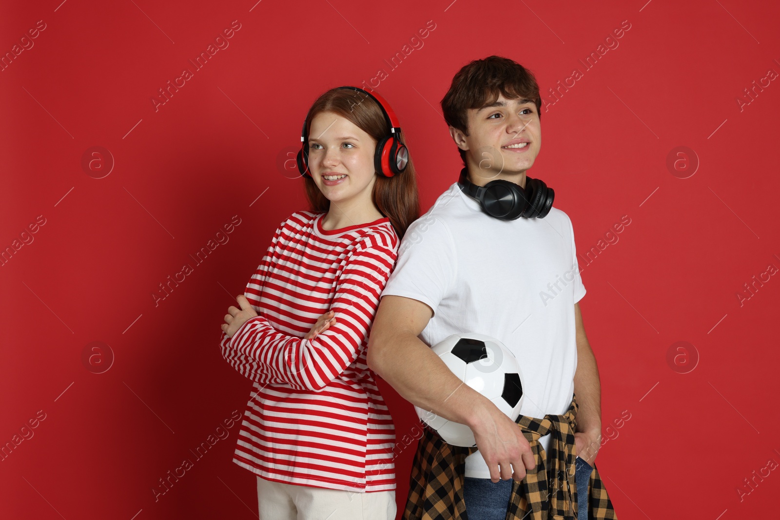 Teenagers with headphones and soccer ball on red background Photo of Teenagers with headphones and soccer ball on red background