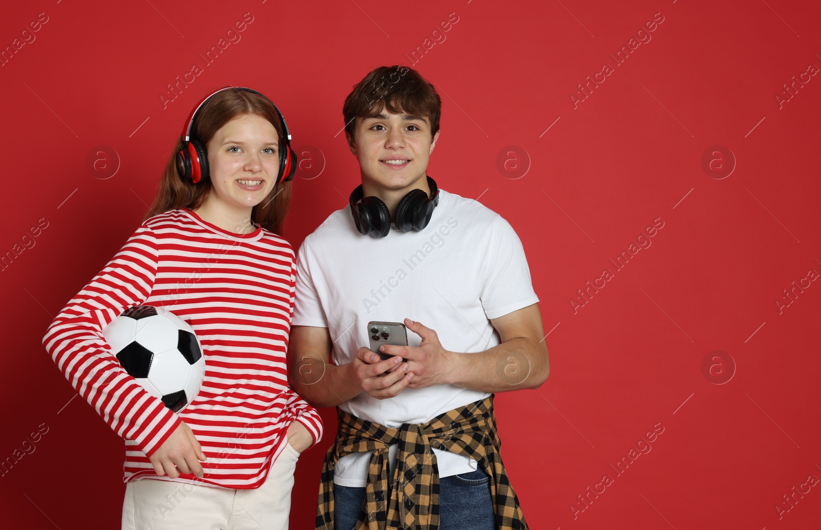 Teenagers with headphones, soccer ball and smartphone on red background Photo of Teenagers with headphones, soccer ball and smartphone on red background