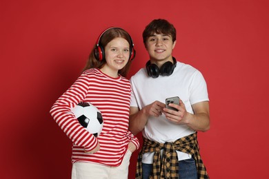 Photo of Teenagers with headphones, soccer ball and smartphone on red background